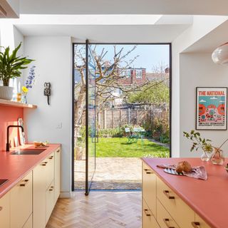 Colourful kitchen units and work surface with glazed pivot door open to the garden