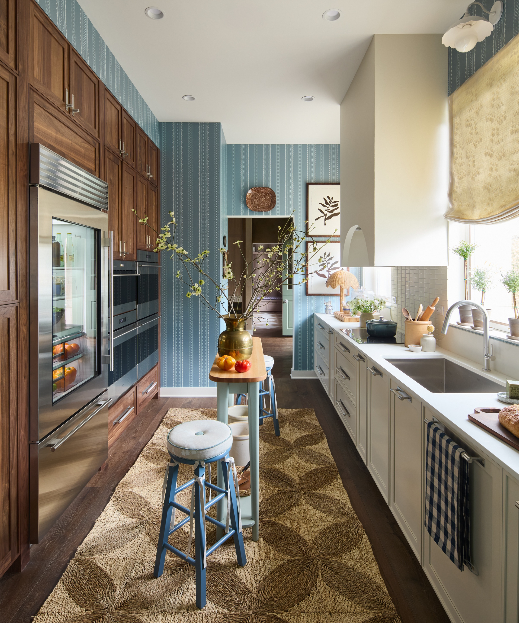 galley kitchen with floor to ceiling cabinets in dark wood on one side, white units on other and striped kitchen wallpaper on end wall