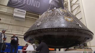 close-up of a cone-shaped spacecraft in a warehouse, with people standing beside it