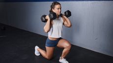 Woman doing a forwards lunge while holding two dumbbells at her shoulders