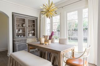 Dining room with wood table, upholstered chairs and bench, dresser, gold pendant light, white walls and wood floor