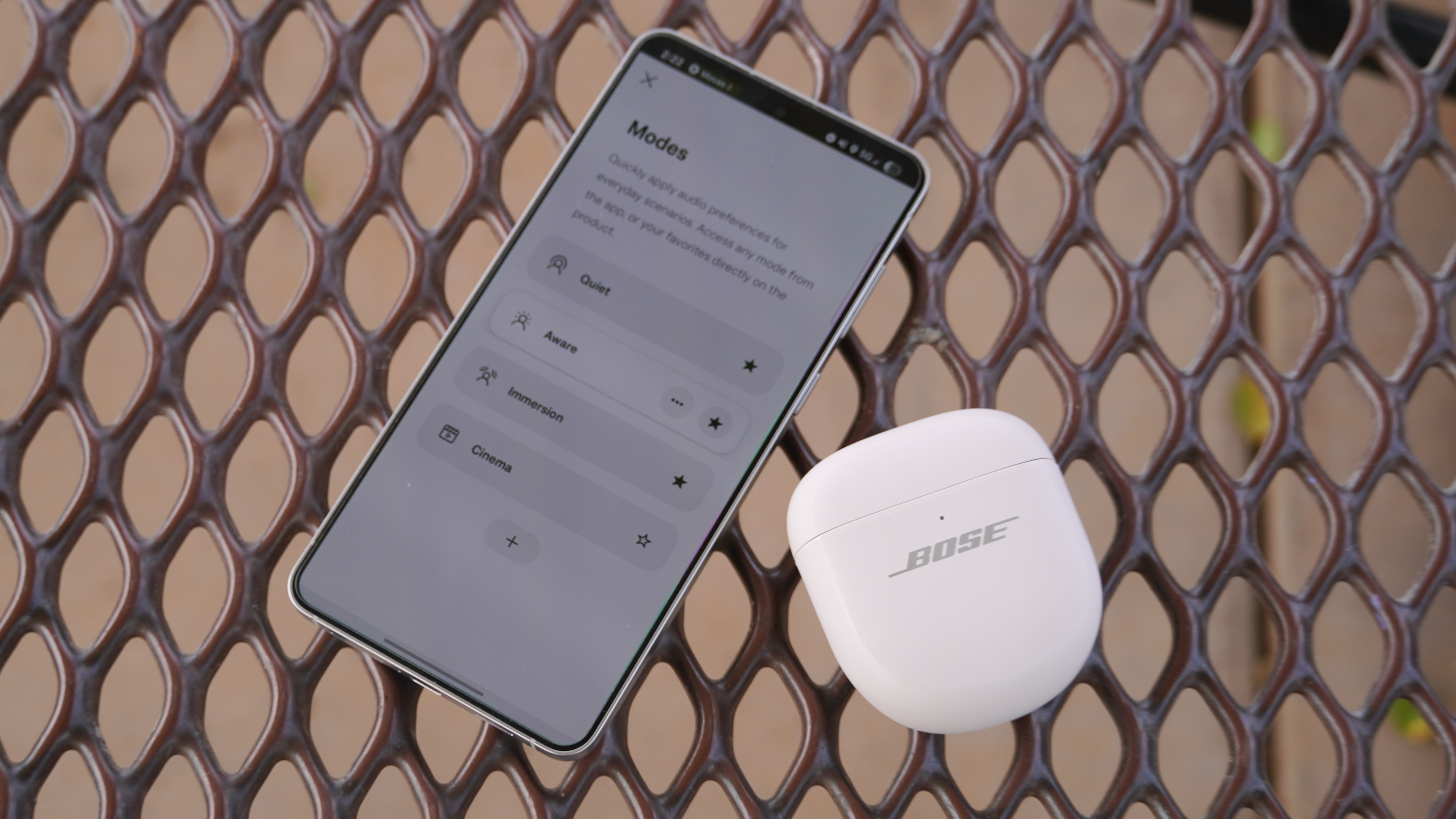 The Bose QuietComfort Ultra Gen 2 earbuds in their case beside a phone with the Bose app open.