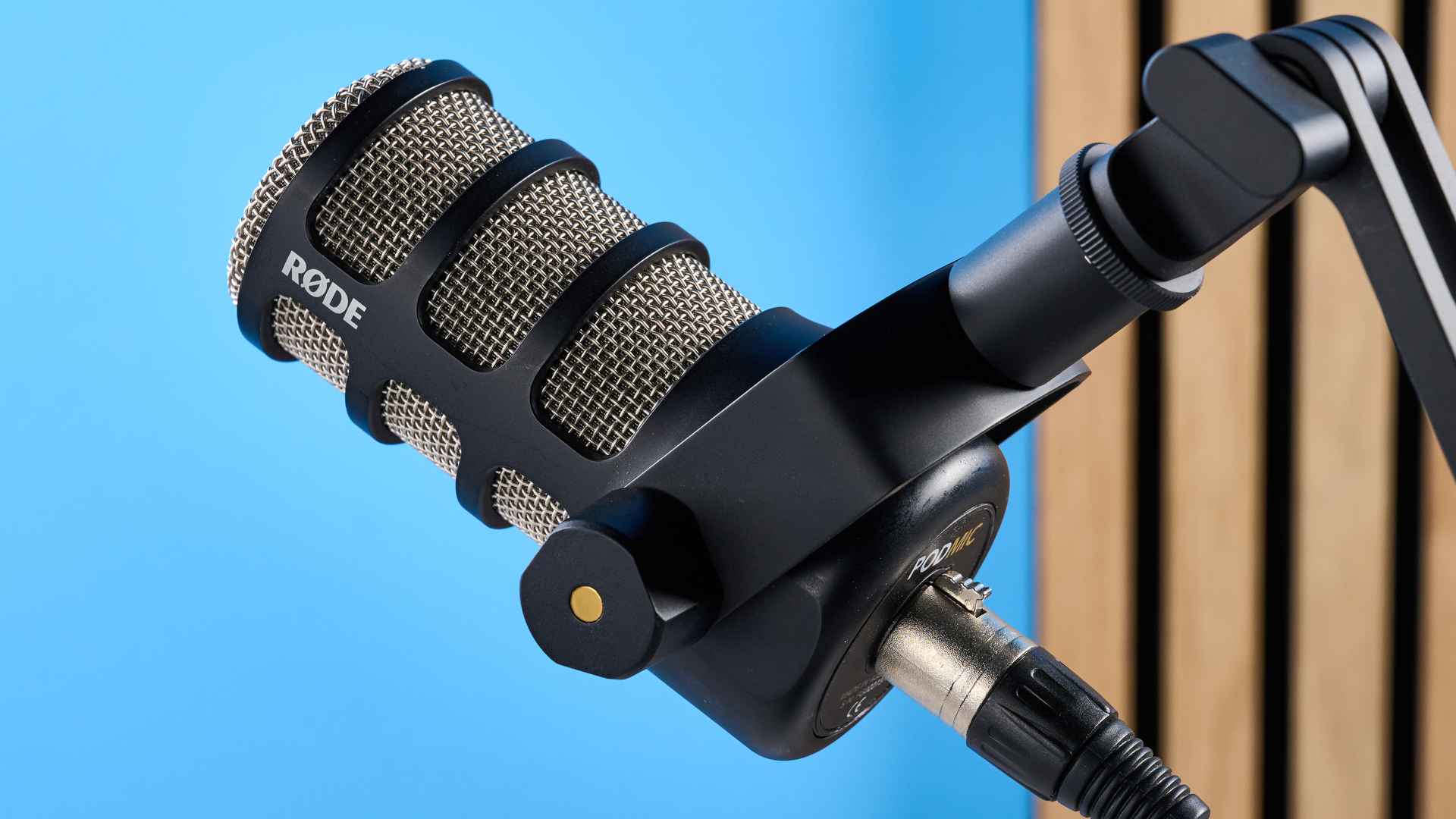 the rode podmic podcast and broadcast microphone photographed with a blue background, shown with the rode ds2 desk stand