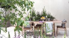 A wooden table and chairs topped with potted plants on a show garden at the RHS Chelsea Flower Show