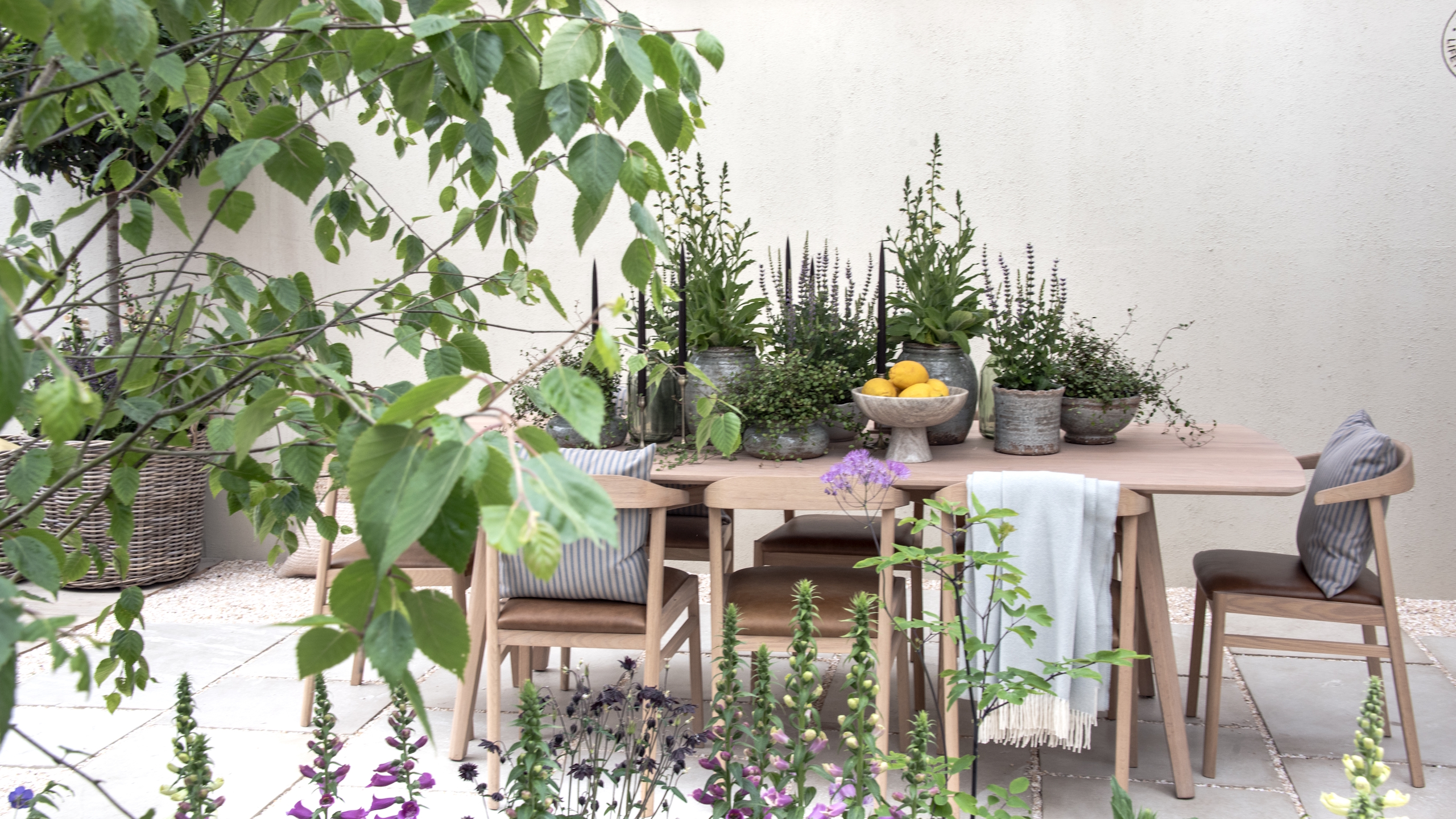 A wooden table and chairs topped with potted plants on a show garden at the RHS Chelsea Flower Show