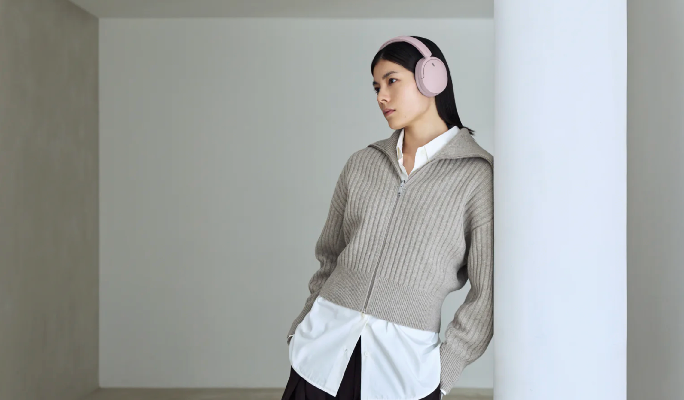 Sony pink WH-CH730N headphones worn by a woman, in a beige room