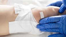 close up on a babies leg as a gloved medical provider places a bandaid on it, as if after a vaccination