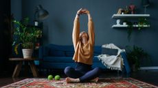 Woman stretching out in living room at home, sitting on rug with fitness accessories, before using core sliders in workout