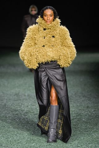 A photo of a model in a brown furry jacket and a black maxi skirt