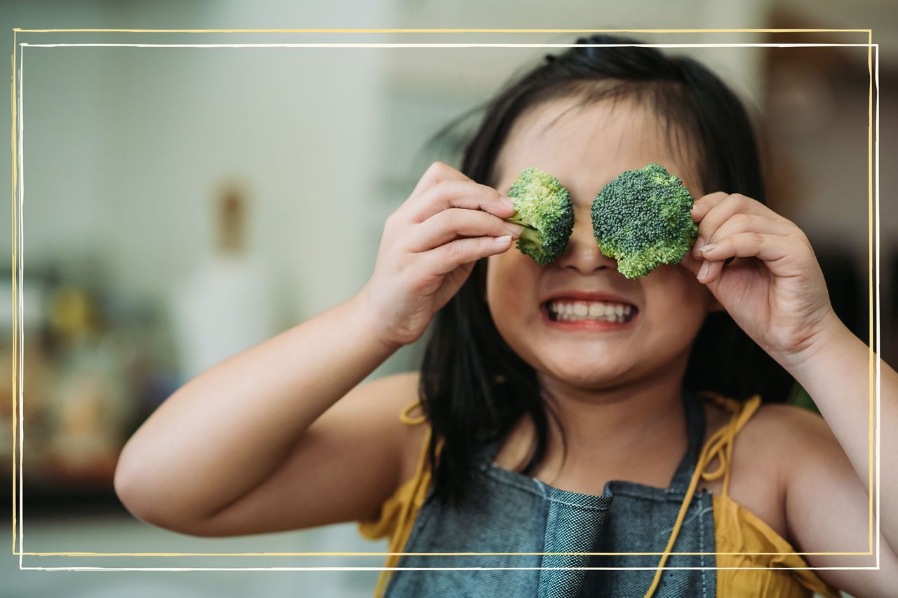 A young girl holding two broccoli florets in front of her eyes 