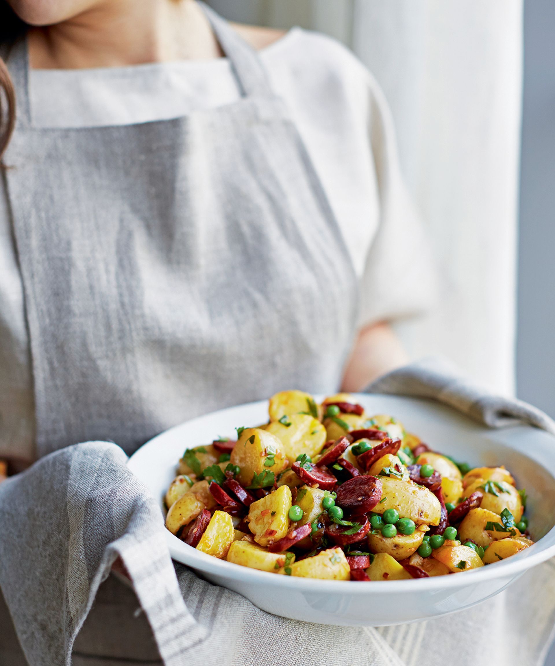Woman holding a white bowl with a potatoes and chorizo dish
