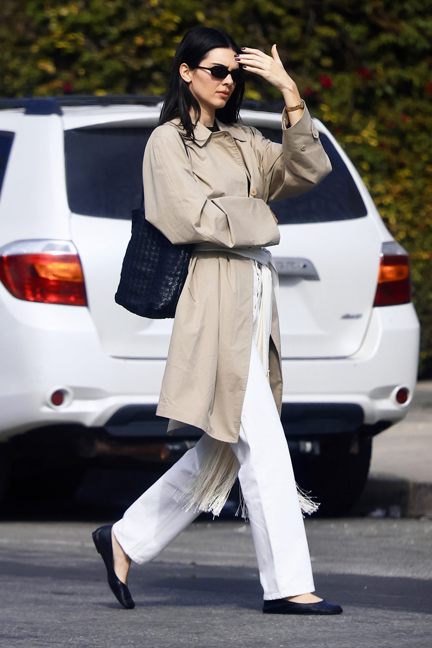 Kendall Jenner wearing a trench coat, scarf belt, white jeans, and black flats