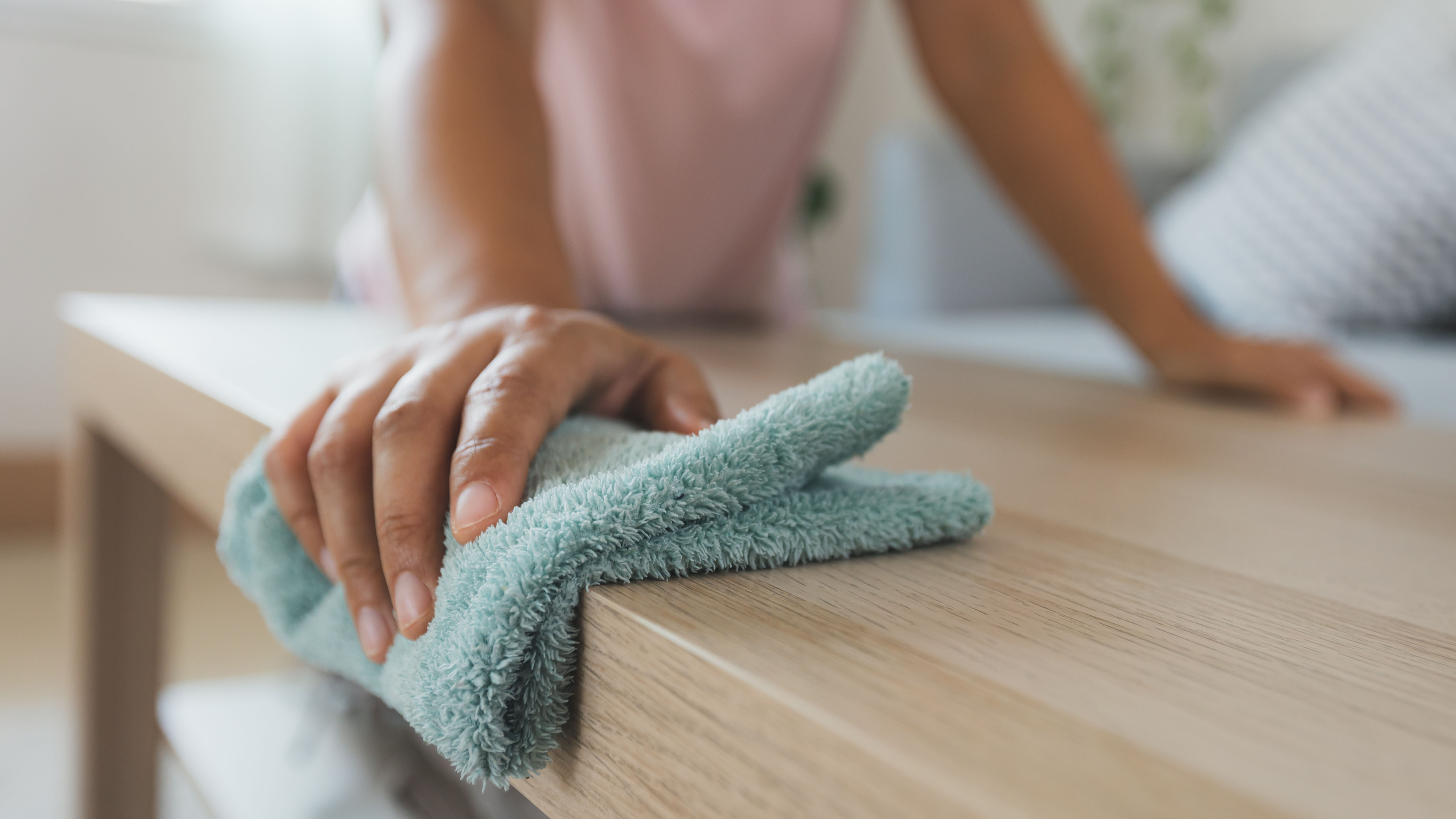 A green microfiber cloth being used to clean wooden surfaces