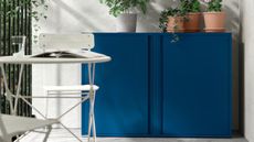 Two IKEA SUNDS&Ouml; outdoor cabinets in cobalt topped with potted plants tucked into the corner of a bright white patio area 