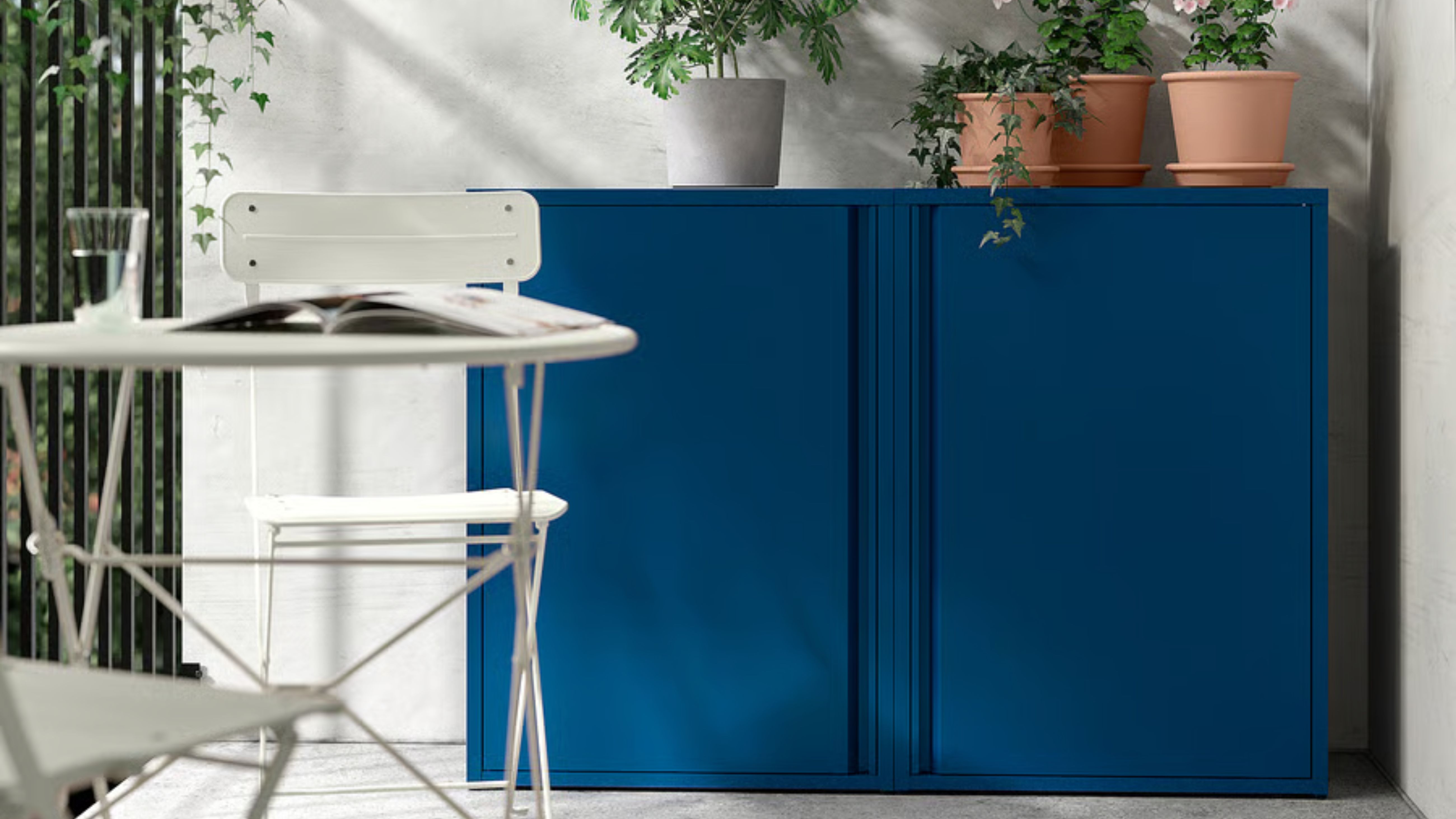 Two IKEA SUNDS&Ouml; outdoor cabinets in cobalt topped with potted plants tucked into the corner of a bright white patio area 