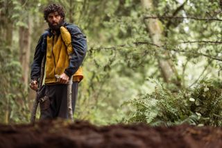 Steven Krueger as Ben Scott in Yellowjackets, episode 2, season 3 wearing a blue and yellow jacket standing with his stick crutches looking at a hole