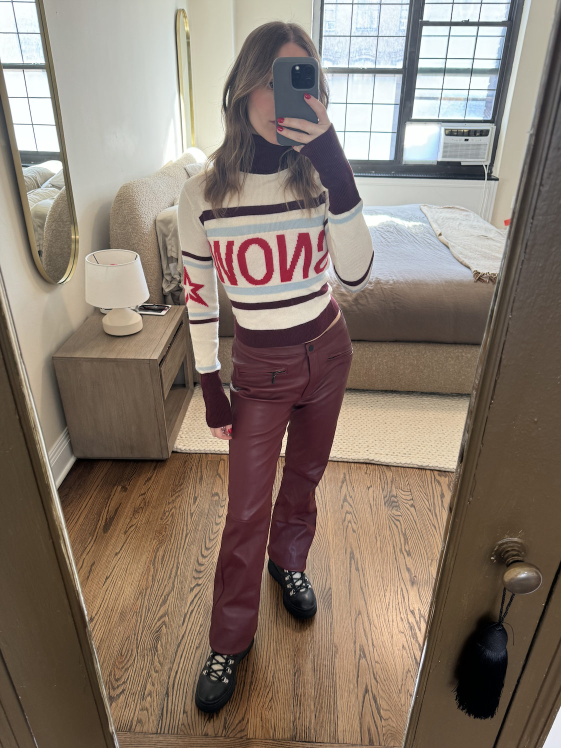 Nikki wears a sweater with "snow" on it and burgundy leather pants.