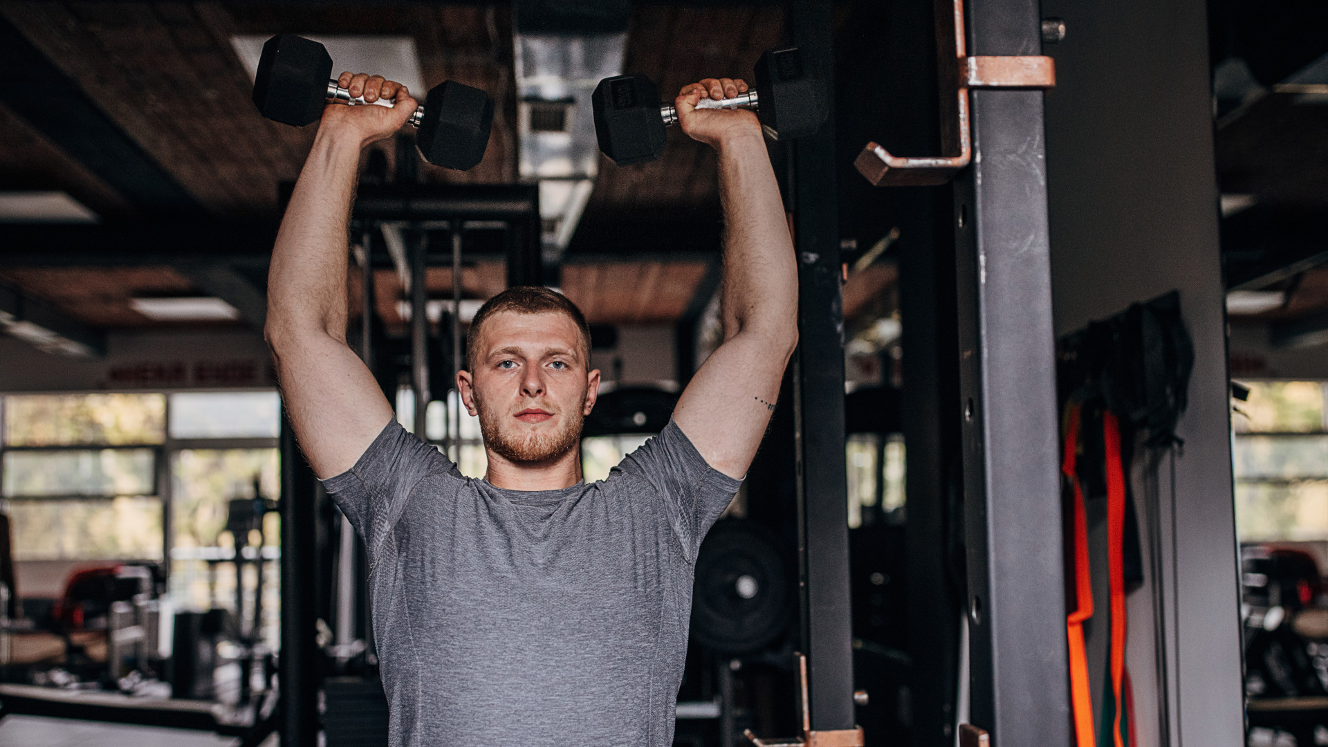 A man performing a dumbbell overhead press in the gym