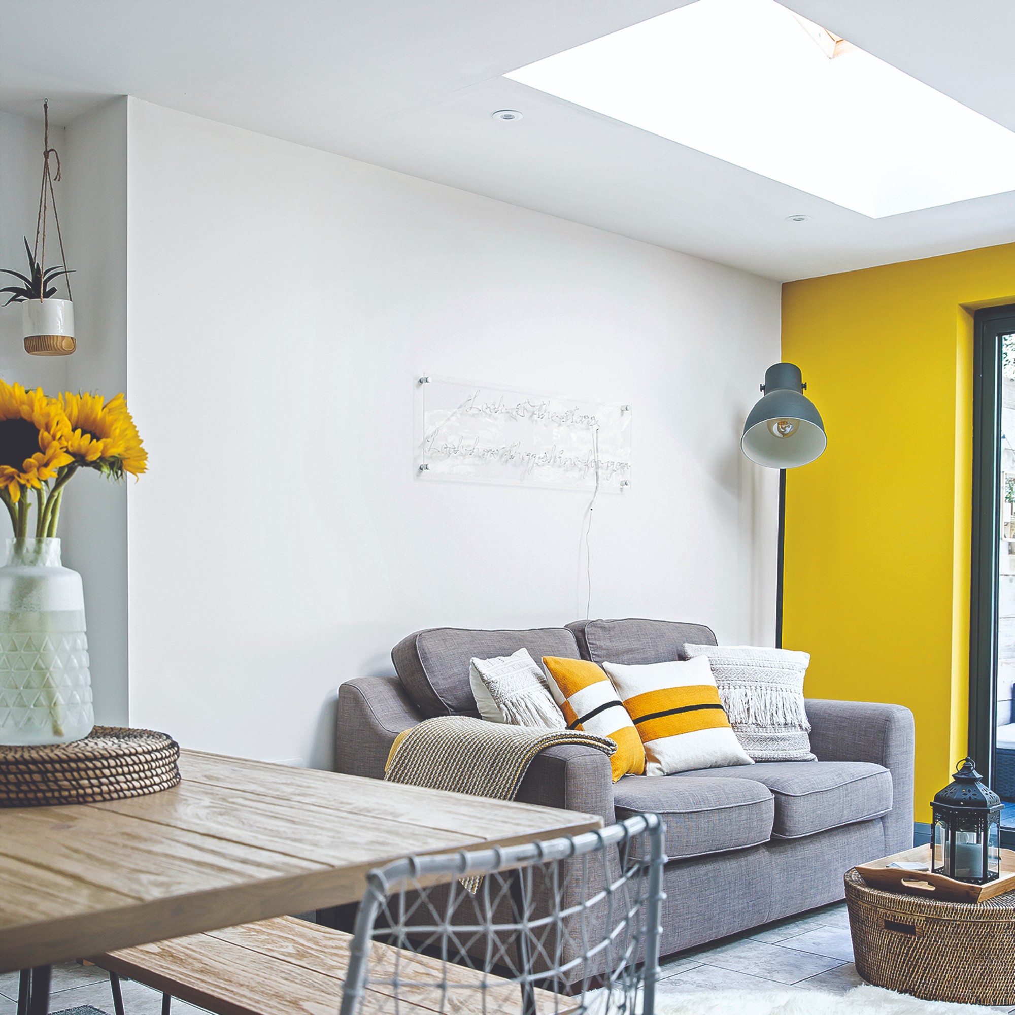 An open-plan living room with a grey sofa, a sky light and a yellow feature wall