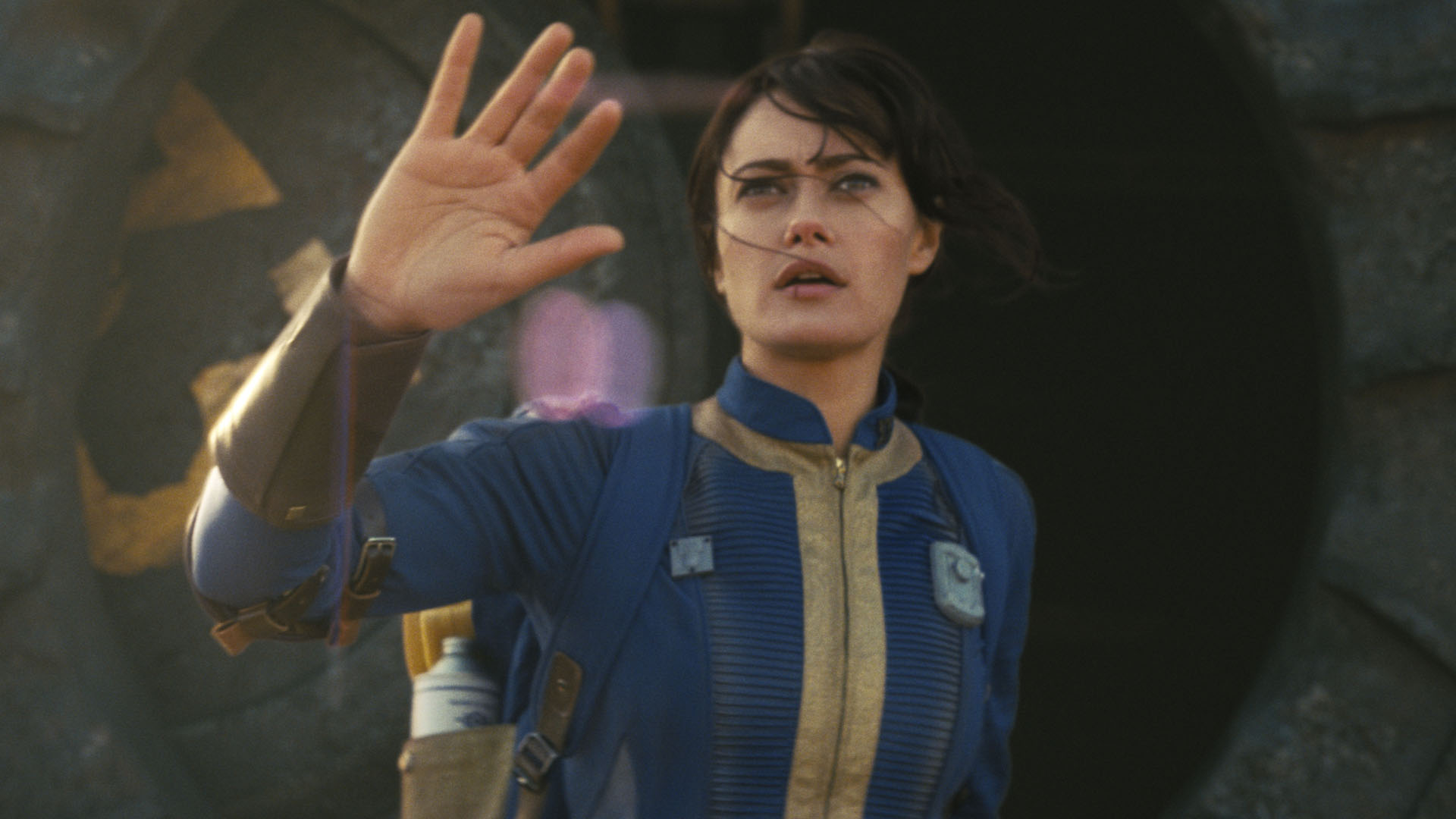 Lucy emerge del Refugio 33 con la mano derecha levantada en el programa de televisión Fallout de Amazon