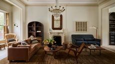 A beautiful modern living room with a wooden rattan chair, a blue sofa, a dusky peach couch, a yellow armchair, a round coffee table, a glass chandelier, a stone mantel over a fireplace