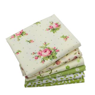 A stack of cream, white, and green fat quarters, with the one on top being cream with a pink and white roses pattern and green polka dots
