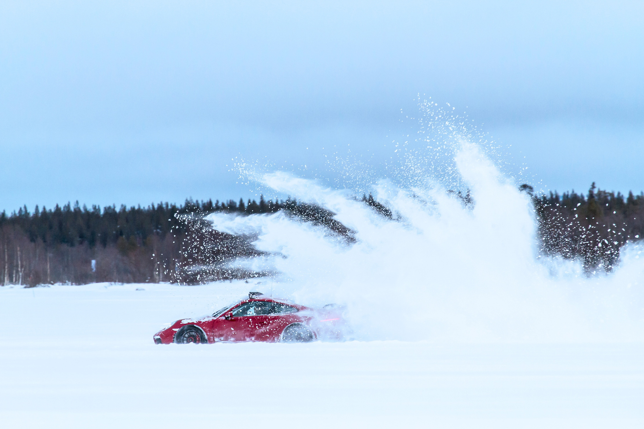 A porsche sprays up some snow behind it as it is being driven across some snow