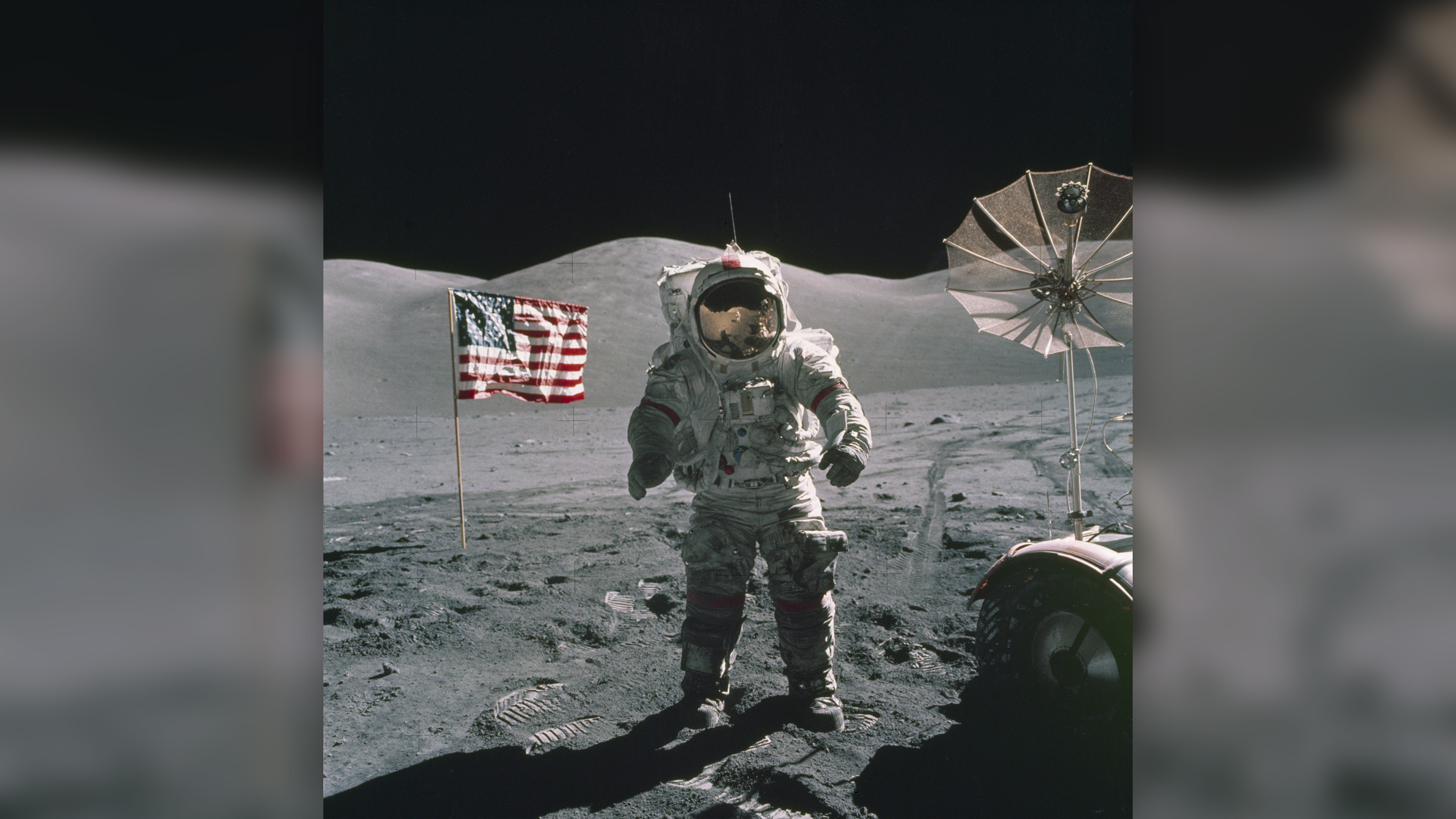 Ein Apollo-17-Astronaut steht auf der Mondoberfläche mit der Flagge der Vereinigten Staaten im Hintergrund.