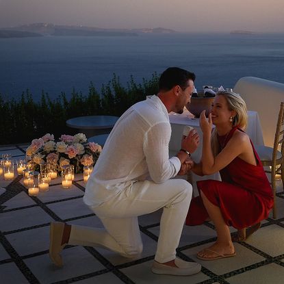Channing Millerd kneeling on one knee proposing to Eliza Spencer next to a table surrounded by candles and roses