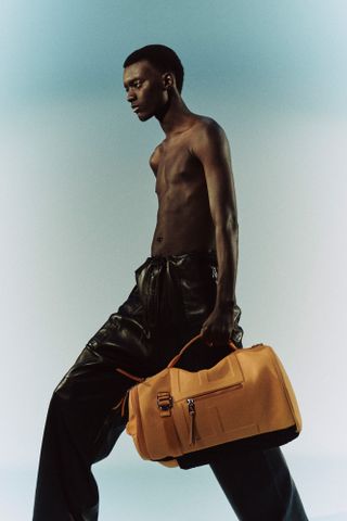 Man with no top wearing trousers and carrying holdall by Fendi