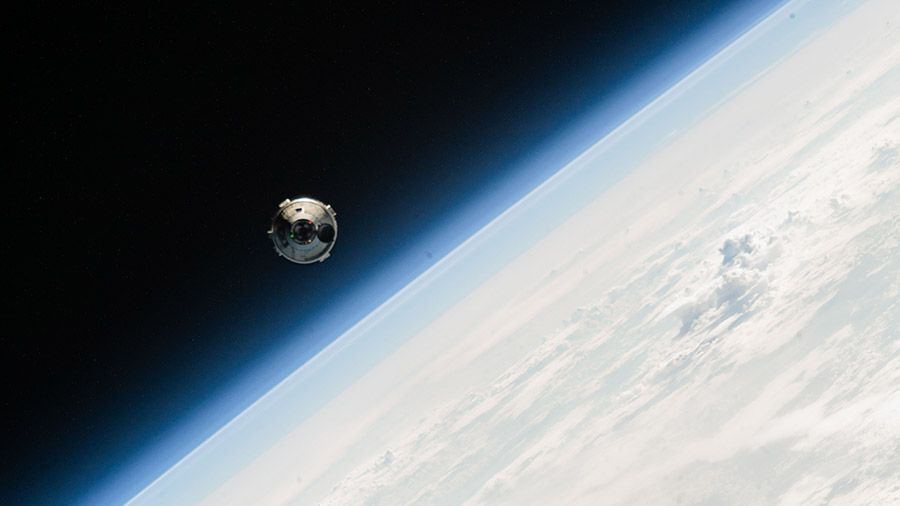 a silvery white space capsule hovers in orbit with earth in the background