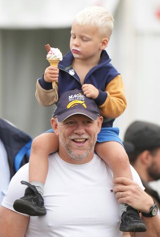 Mike Tindall wearing a baseball hat and T-shirt holding his son on his shoulders eating an ice cream