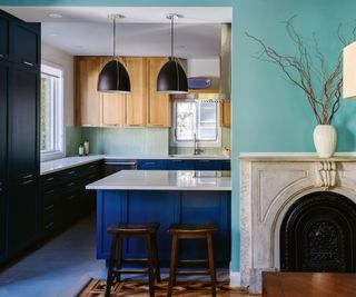 A blue kitchen island with a marble countertop designed to fit around a chimney