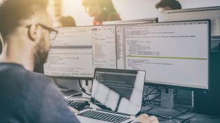 A man with glasses looking at several screens with code on them