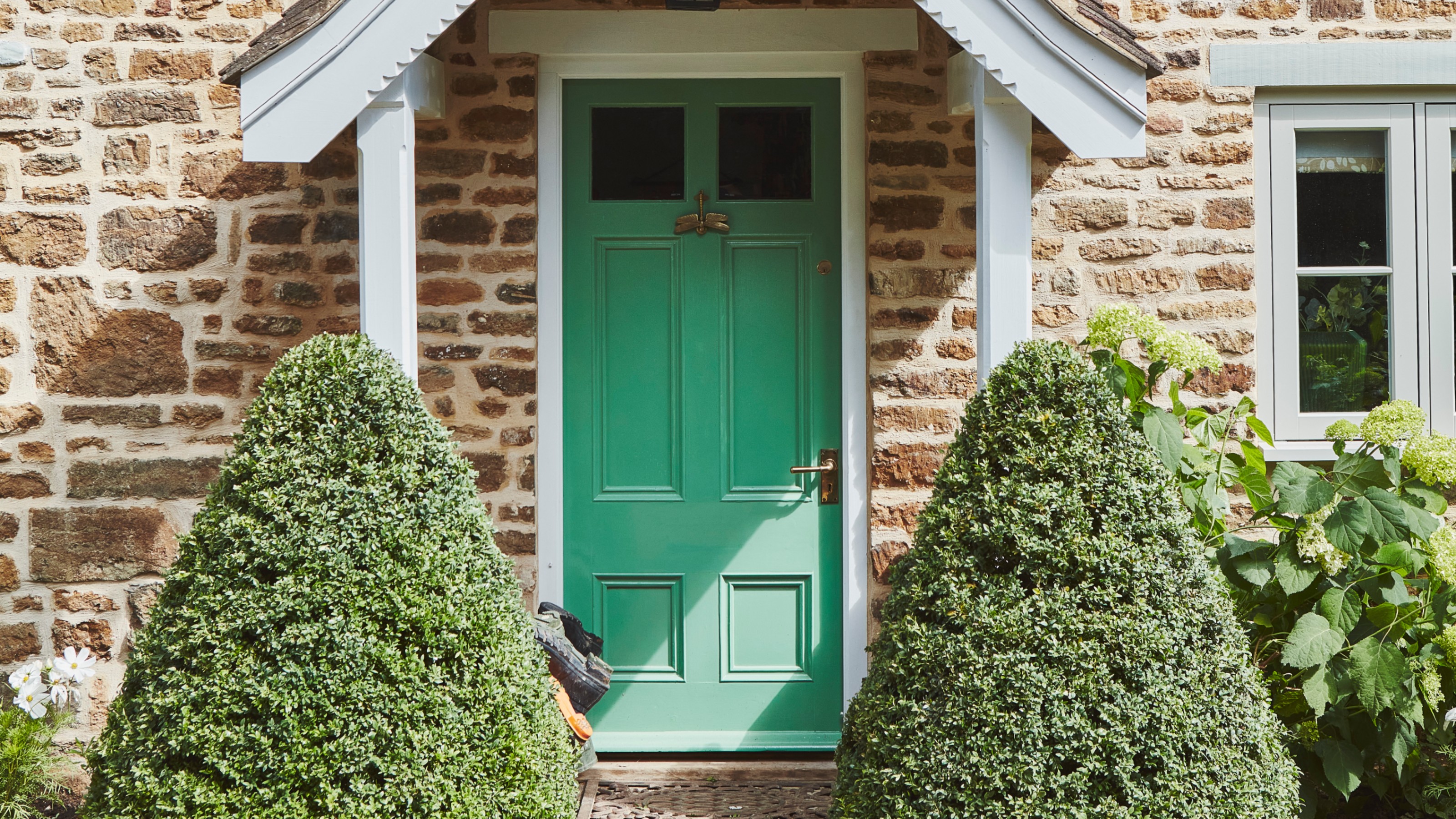 A country house with a mint green front door with a brass door handle and a dragonfly door knocker with a porch