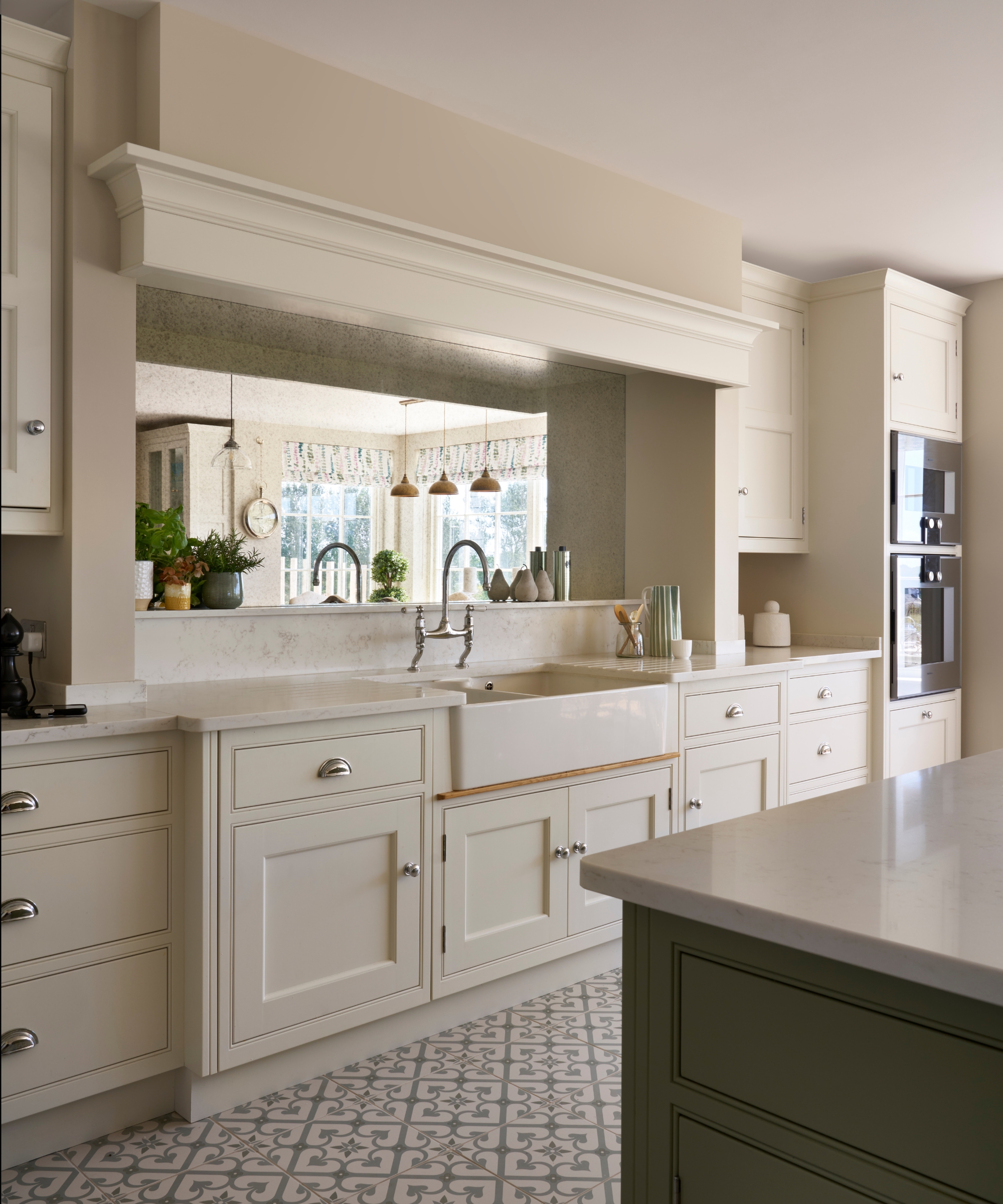 A white kitchen with a green island and a mirrored backsplash