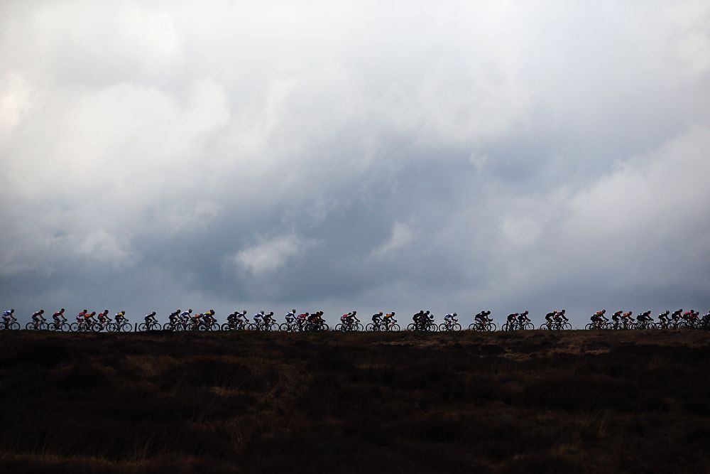 The peloton single file under threatening rain clouds