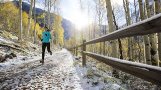 A woman runs on a snowy trail in Autumn with yellow aspens behind her