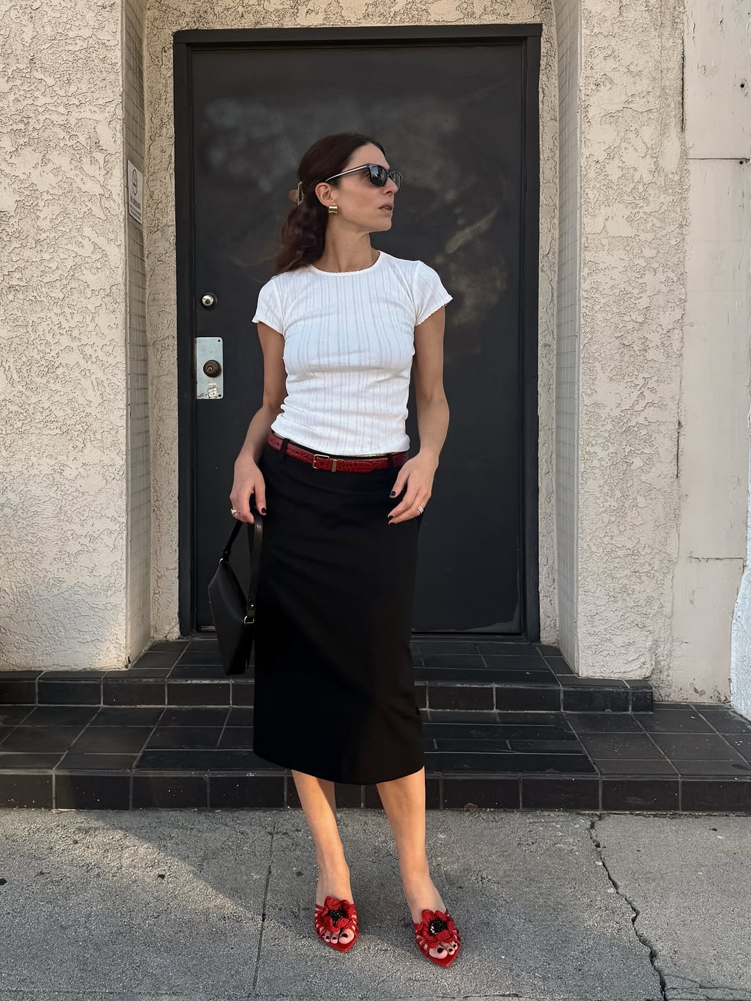 An image of woman wearing red shoes, one of the biggest 2026 shoe color trends, with white t-shirt and black skirt.
