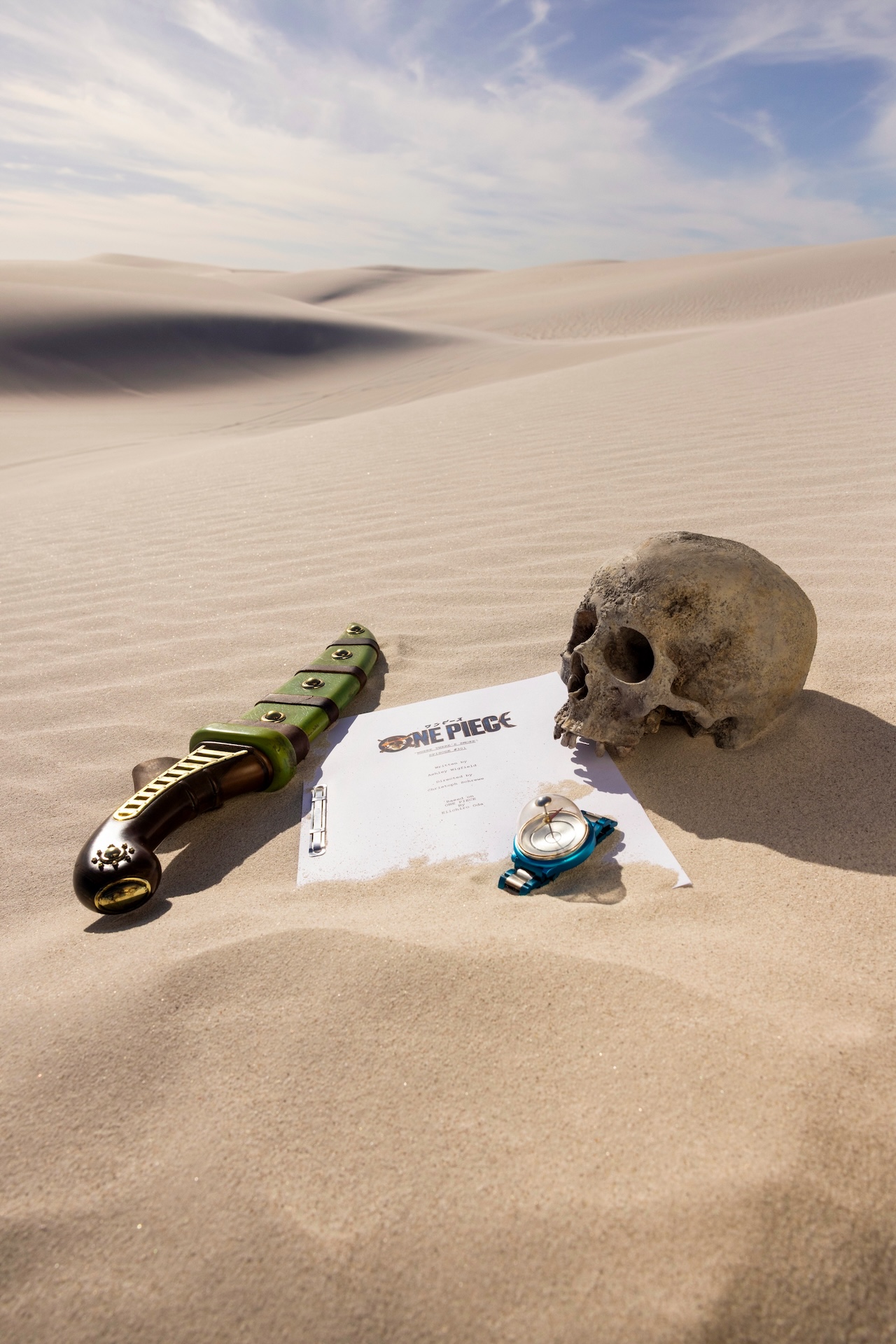One Piece Season 3 premiere script sitting out in desert alongside a human skull, Log Pose and a distinctive dagger