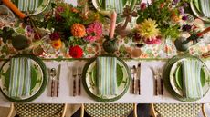 floral summer table styled with a floral tablecloth, lots of bud vases of fresh bright flowers, candles, and green woven placemats with white and green plates