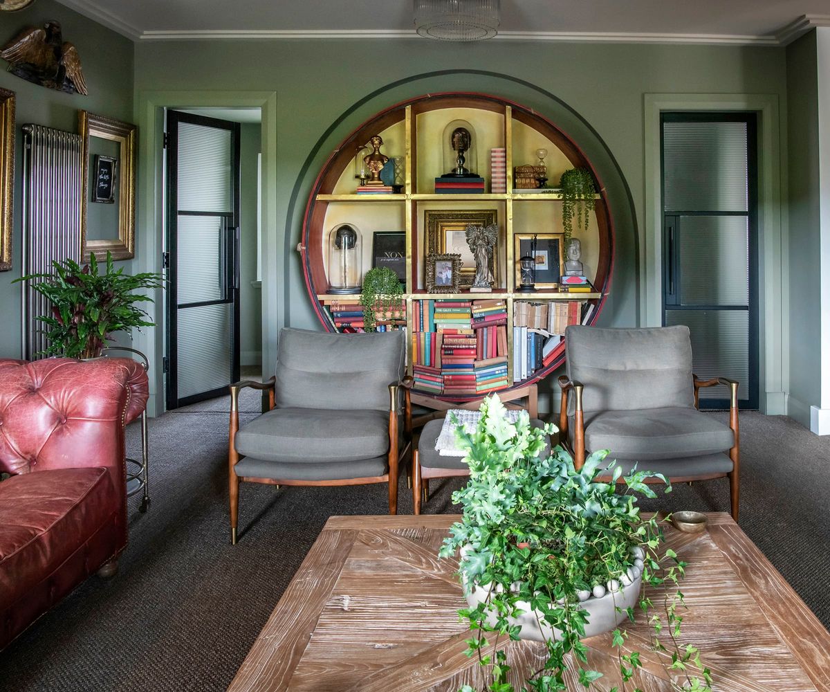 A living room with a circular bookcase and grey carpet and red leather sofa
