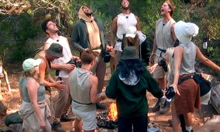 a group of people scream while standing around a campsite, in 'surviving paradise'