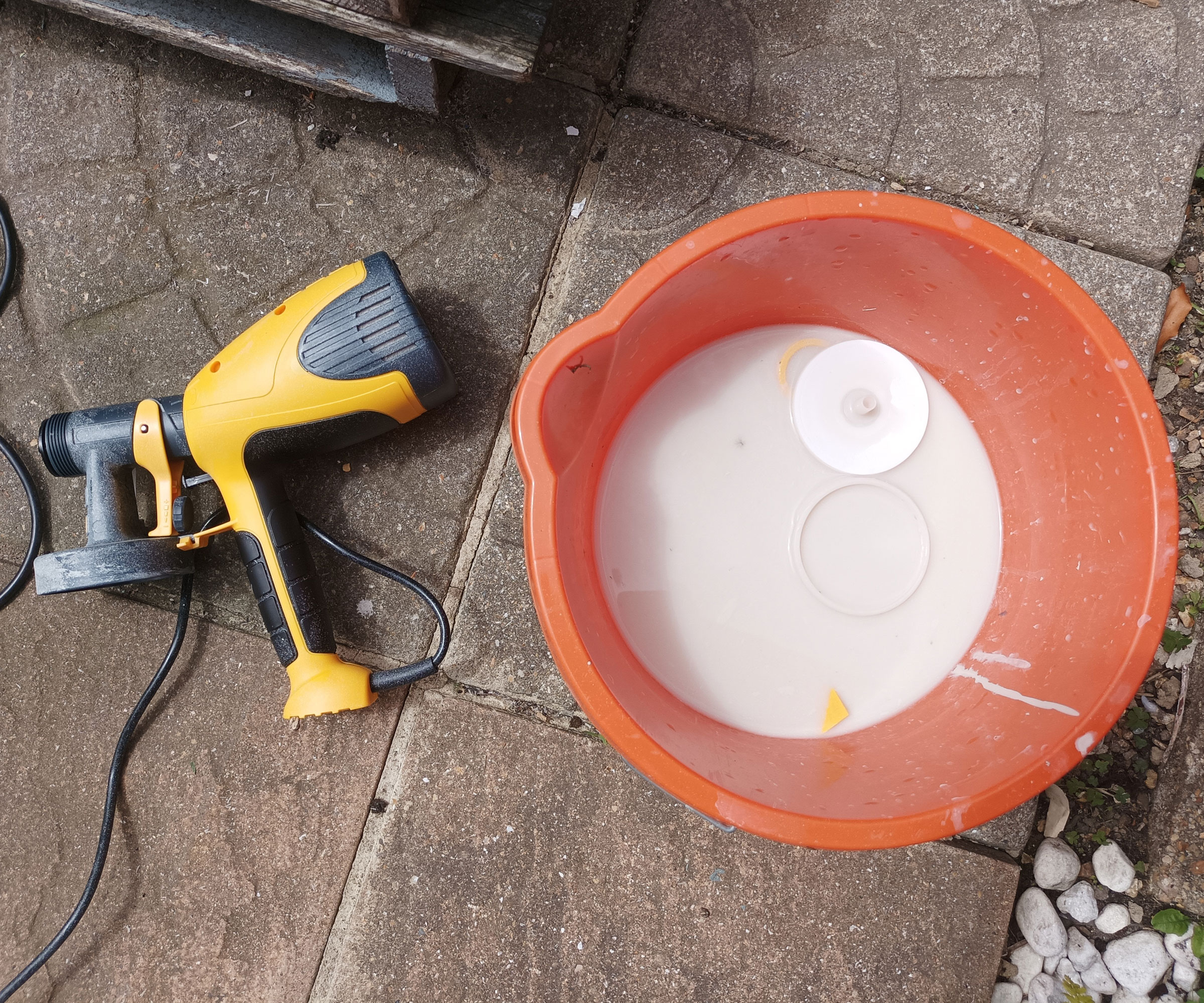 Top down shot of yellow paint spray gun and orange bucket with white water on paving slabs