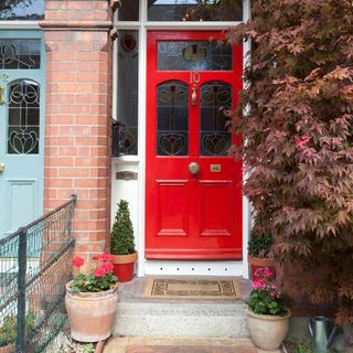 red front door with plants and shrubs with brick column