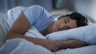 A man in a blue t-shirt sleeps on a cooling pillow