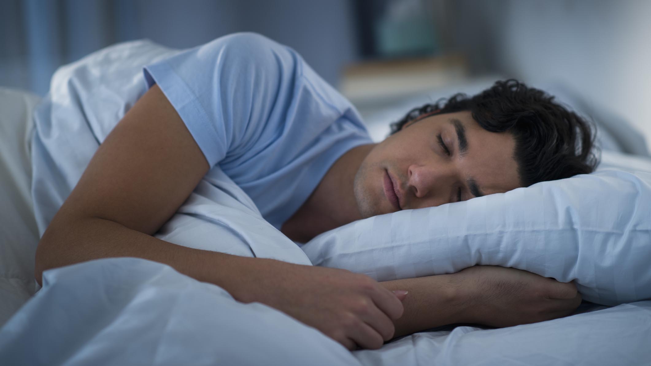 Как исправить свой режим сна: мужчина в синей футболке спит на белой подушке