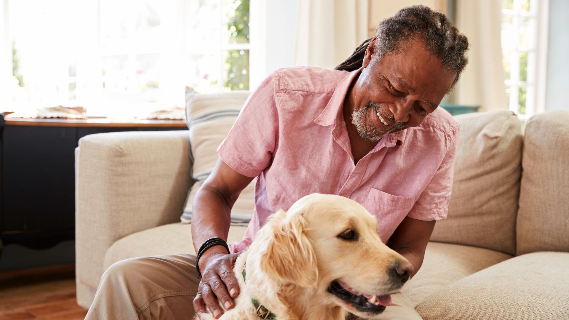 An older man relaxes at home on the couch with his golden retriever dog at his feet.