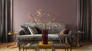 living room with dark pink walls, grey curtains and sofa, coffee table with pink vase and large sprigs of foliage