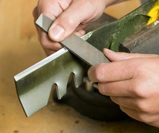A close up on hands sharpening lawn mower blades with a file